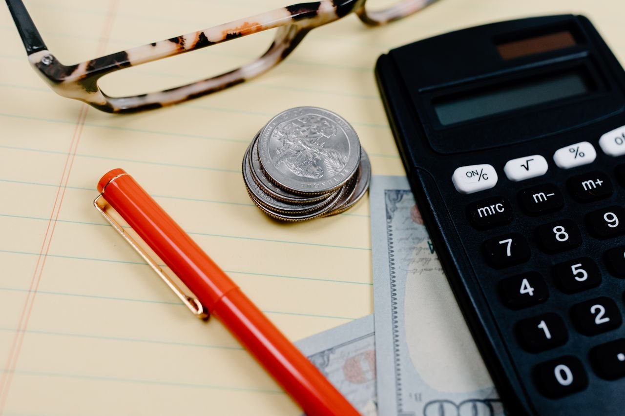 Calculator, pen and coins on a notepad for catching up on overdue bookkeeping in Ontario